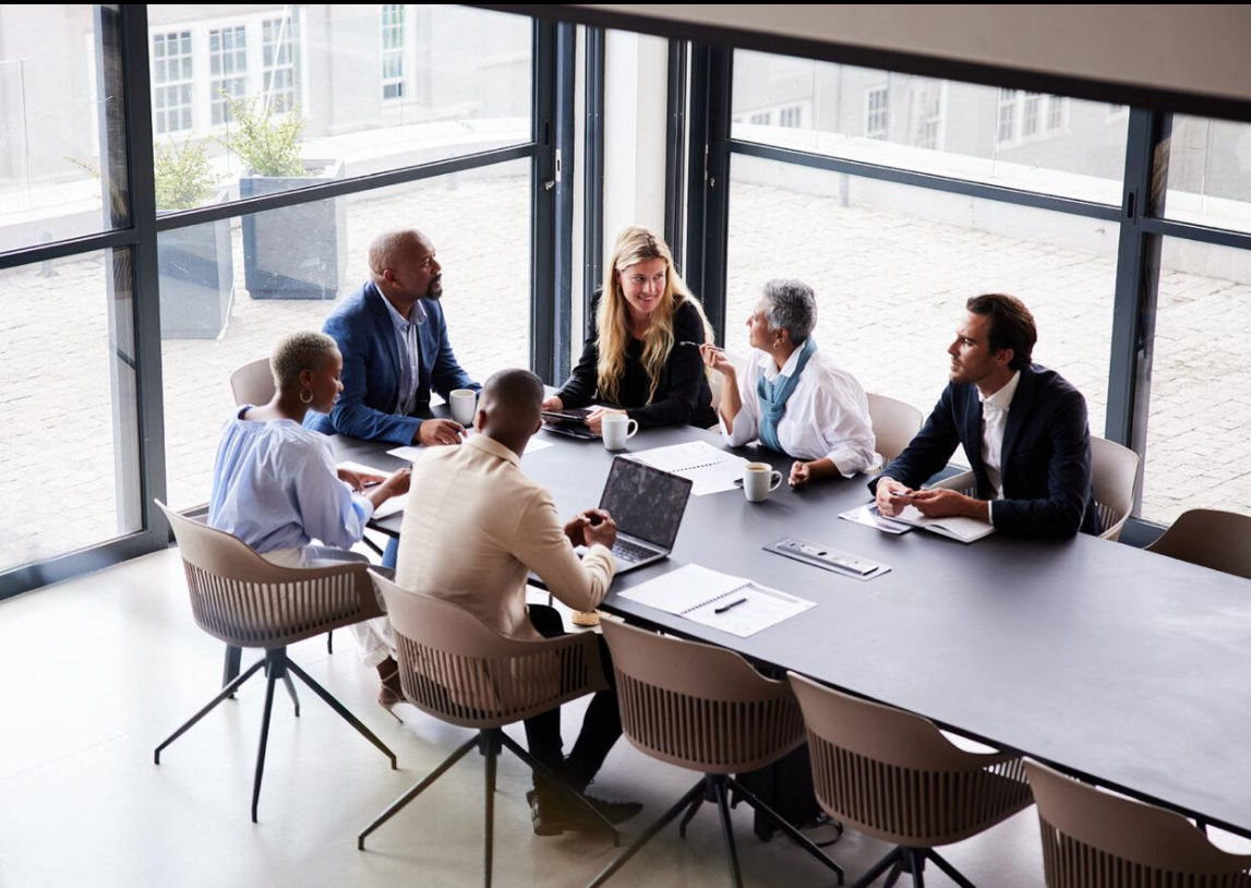 Diverse leadership team in conversation around a long table in a light-filled office